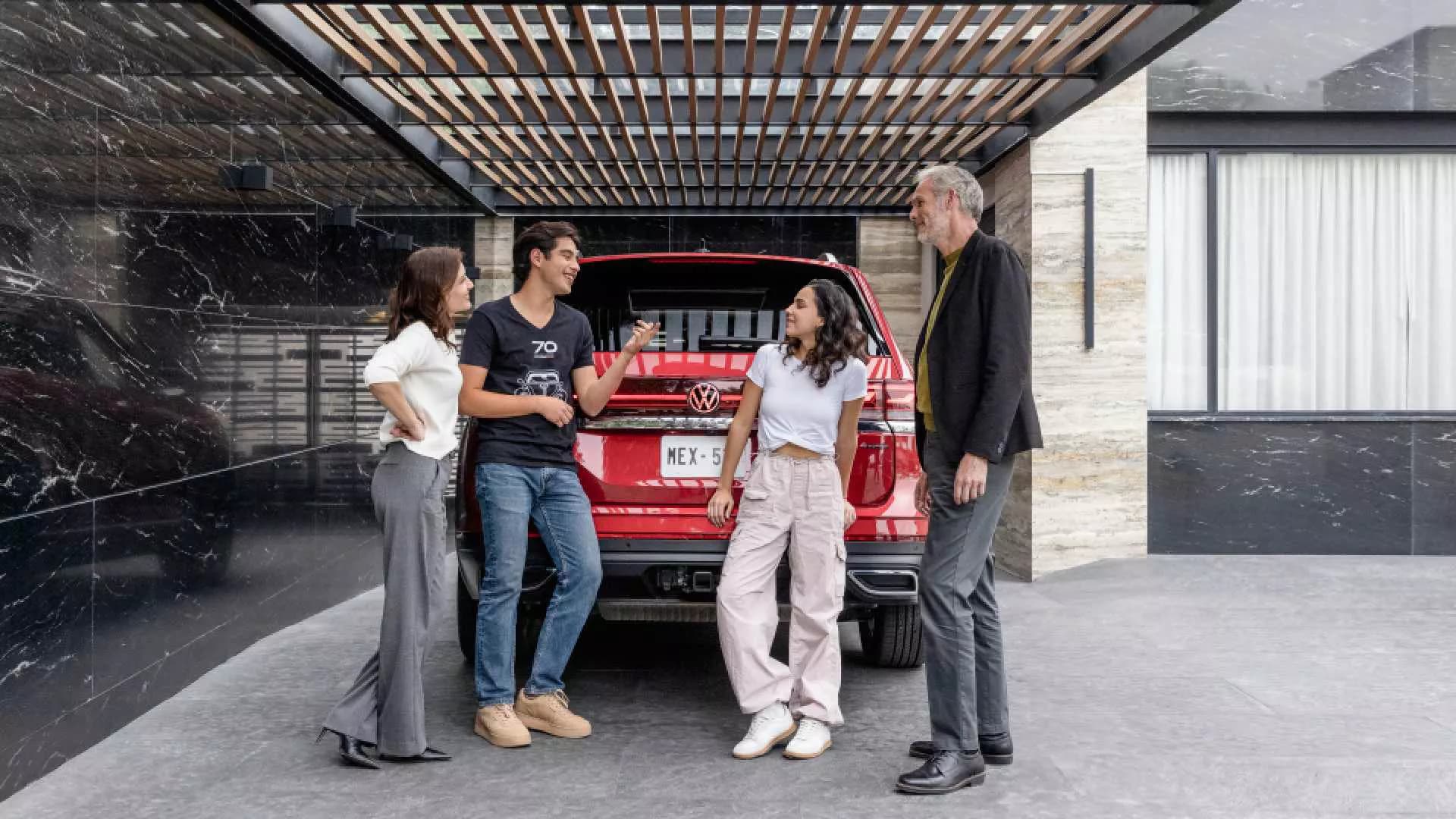Cuatro personas conversan de manera relajada junto a un automóvil